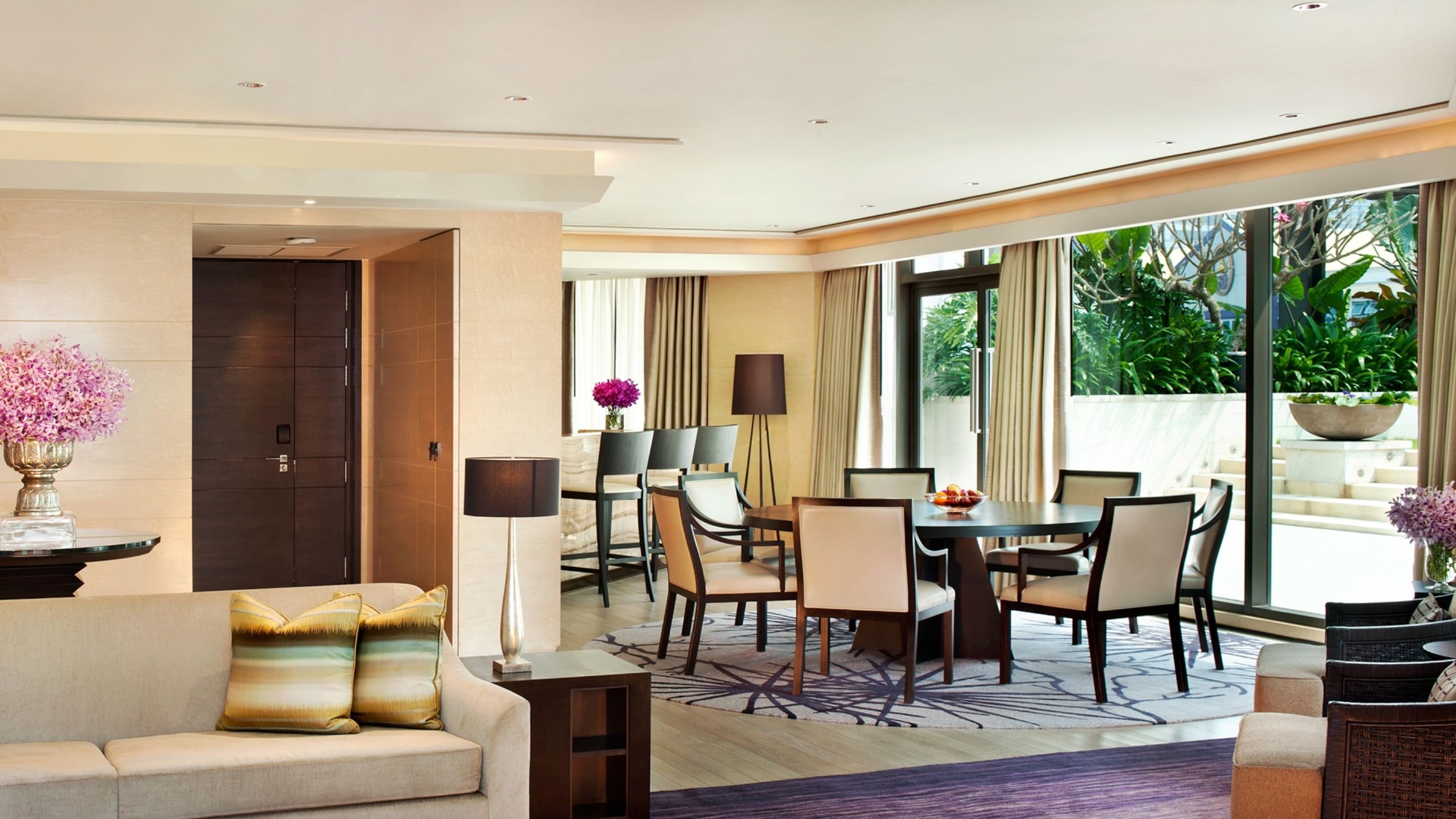 Habitación de hotel moderna con sofá, mesa de comedor, sillas y vistas a zonas verdes.