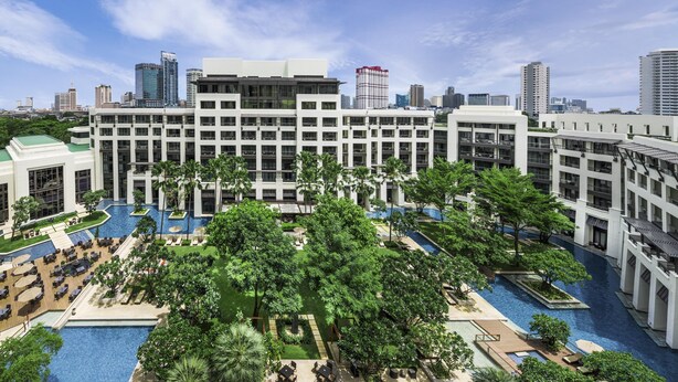 Un hôtel moderne doté de plusieurs piscines, d’une végétation luxuriante et offrant une vue sur les gratte-ciel de la ville en arrière-plan.