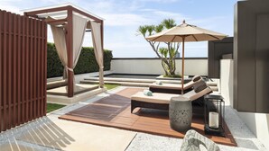 Une terrasse sur le toit avec une plateforme en bois, un coin salon avec des coussins, une pergola avec des rideaux et un petit jardin agrémenté de palmiers.