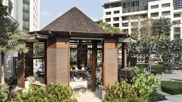 A modern outdoor seating area with a wooden pergola, surrounded by lush greenery and a well-maintained lawn.