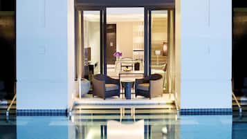 A hotel lobby with a pool, two armchairs, a table, and a vase of flowers.