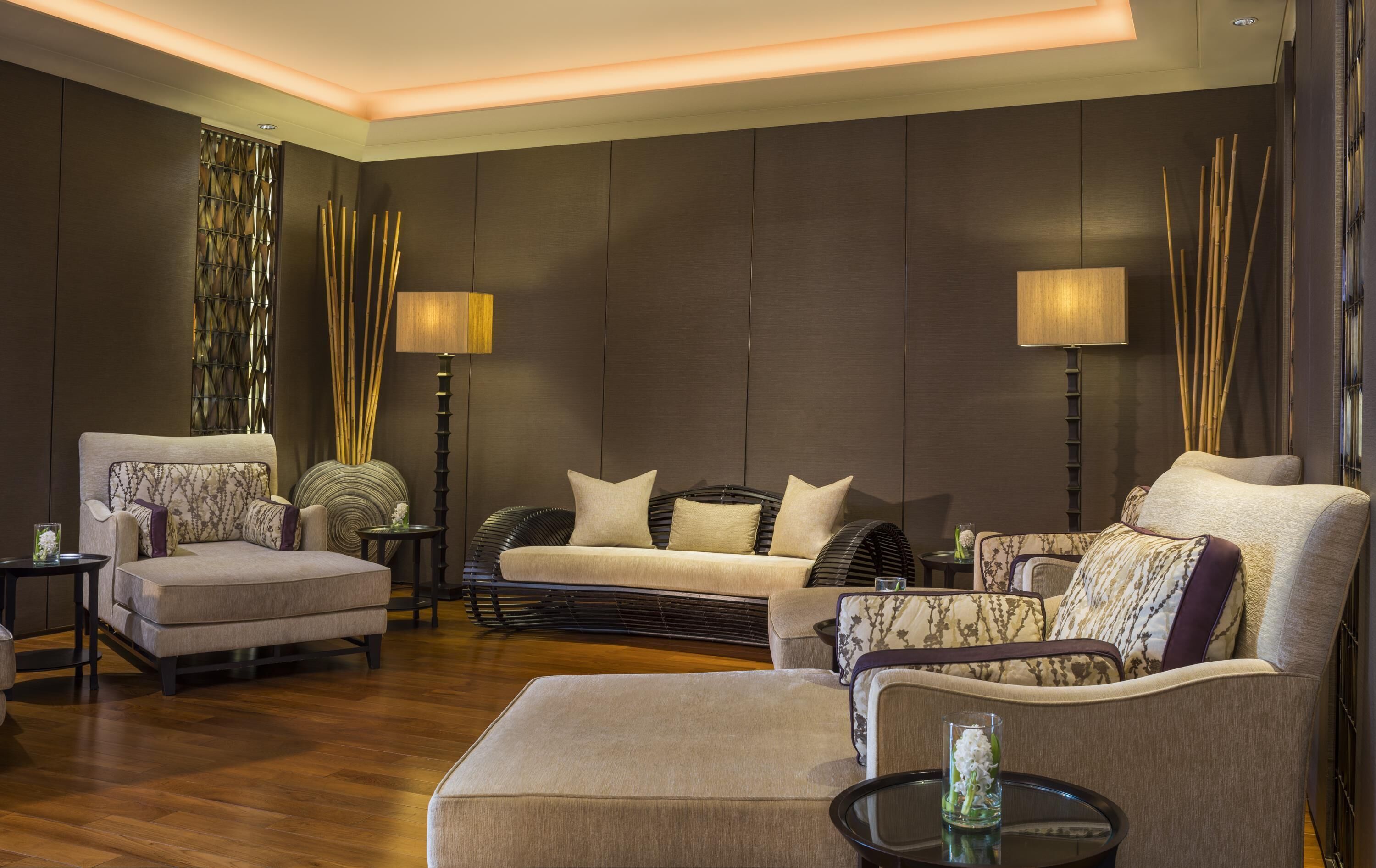 Una sala de estar moderna con paneles de madera oscura, un conjunto de sofá color beige y dos lámparas de pie.