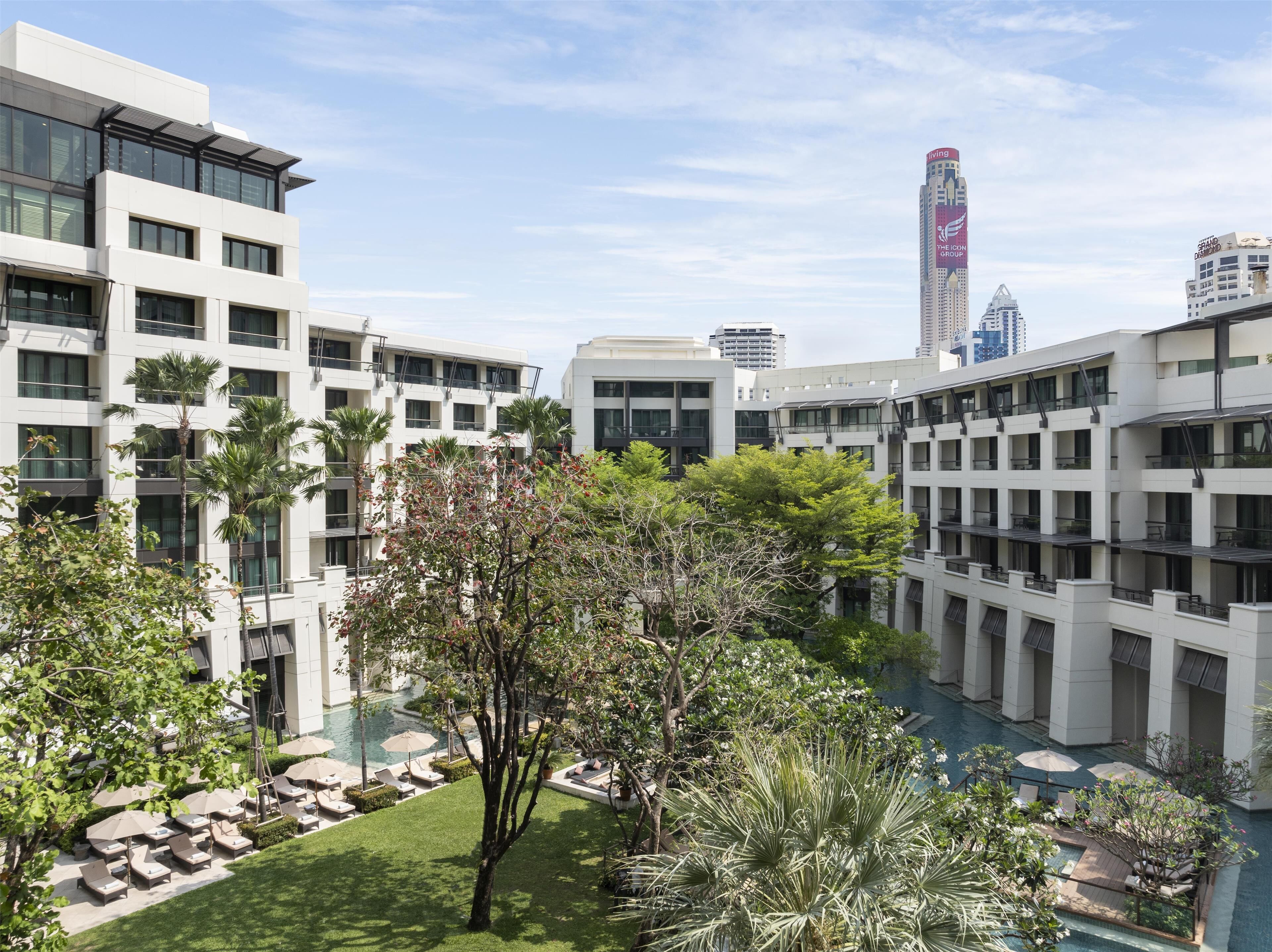 A modern hotel courtyard with a pool, palm trees, and a view of surrounding high-rise buildings.