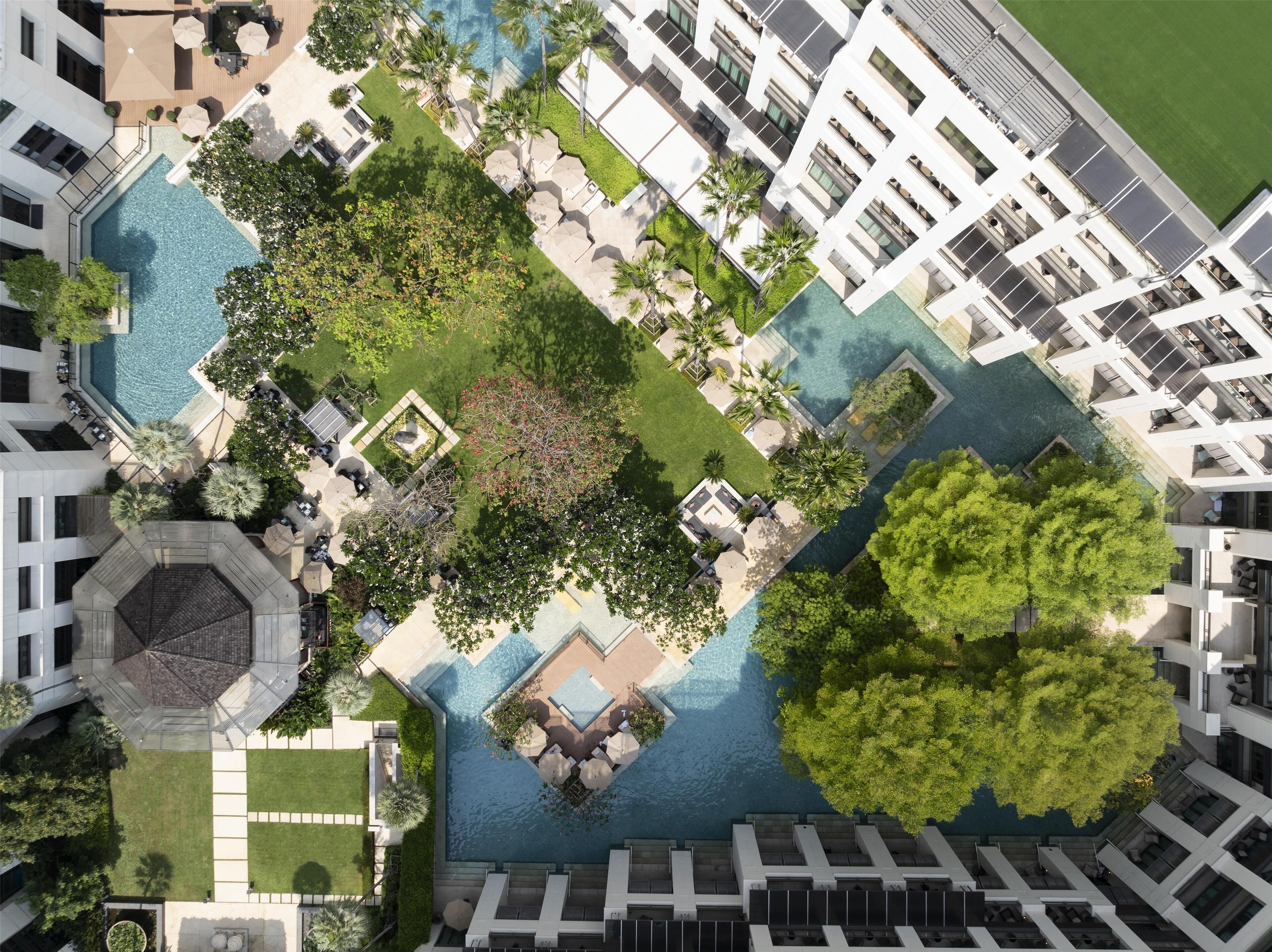 An aerial view of a hotel with multiple swimming pools, lush greenery, and modern architecture.