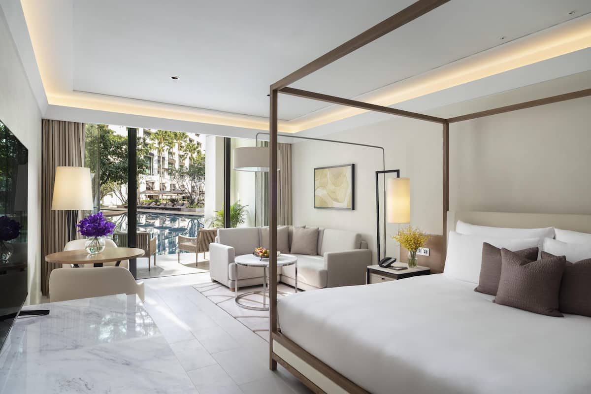 Ein modernes Hotelzimmer mit Himmelbett, einem Balkon mit Pool und einer Sitzecke mit Tisch und Stühlen.