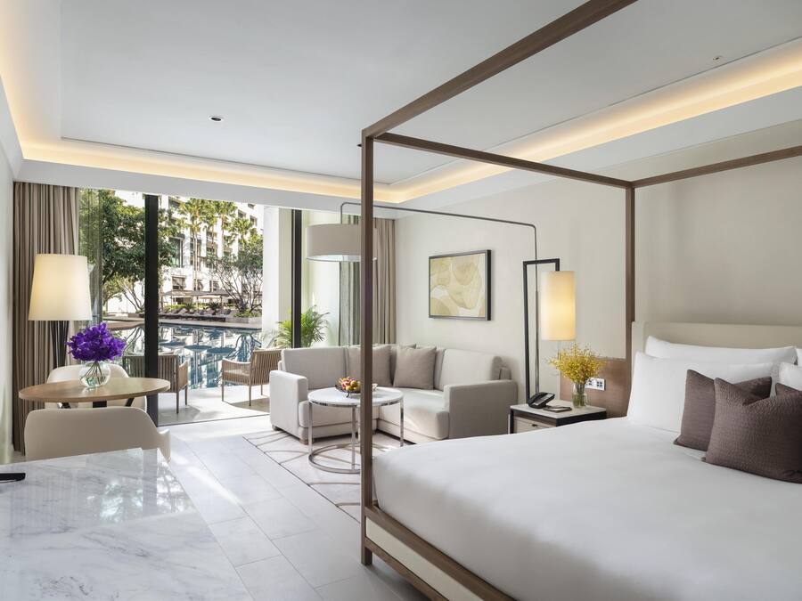A modern hotel room with a four-poster bed, a balcony with a pool, and a seating area with a table and chairs.