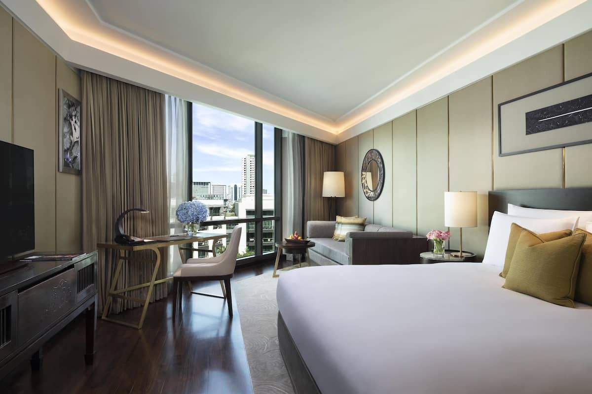 Ein Hotelzimmer mit einem großen Bett, einem Schreibtisch mit Stuhl, einem Fernseher und Blick auf die Stadt.