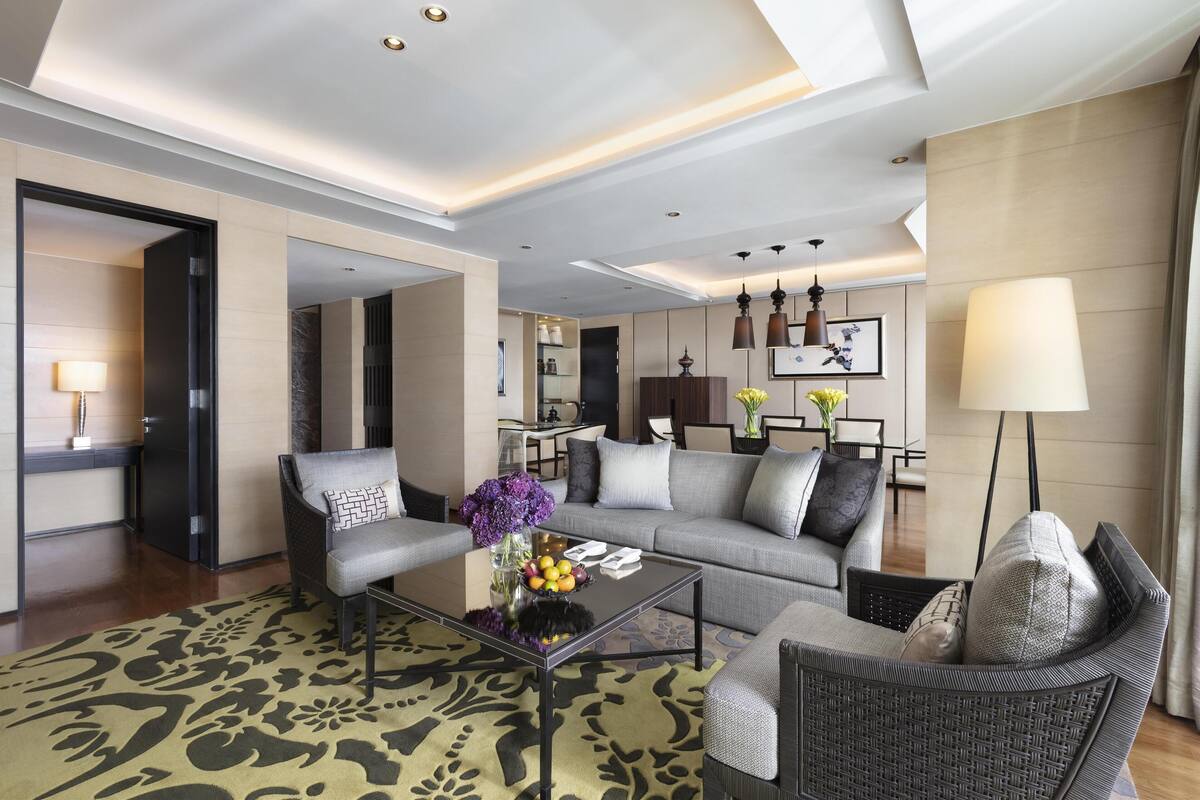 Ein modernes Hotelzimmer mit einer Couch, Sesseln, einem Glastisch und einem Essbereich mit Tisch und Stühlen.