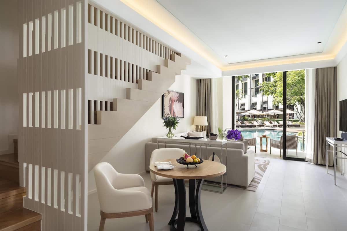 Ein modernes Wohnzimmer mit Treppe, einem Essbereich mit Tisch und Stühlen, einer Couch und Blick auf einen Poolbereich im Freien.
