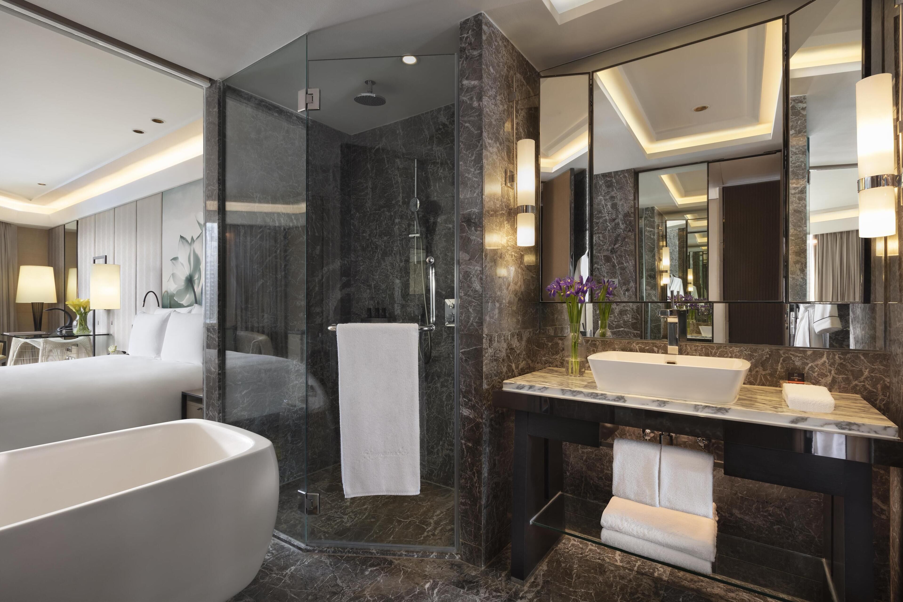 A modern bathroom with a large bathtub, a glass-enclosed shower, and a marble vanity with a sink and mirror.