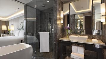 Une salle de bain moderne dotée d’une grande baignoire, d’une douche à parois de verre et d’un meuble-lavabo en marbre avec un évier et un miroir.