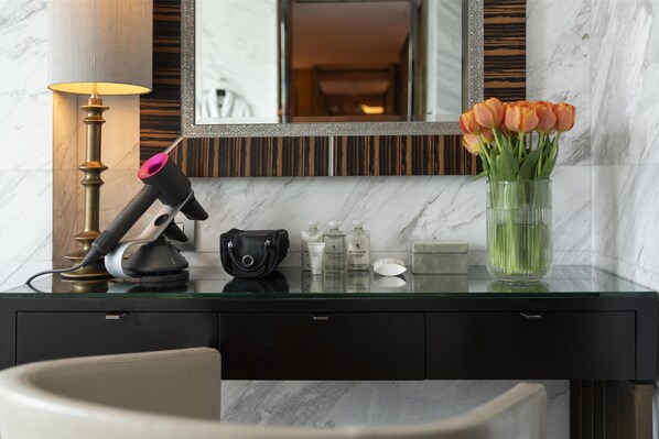 A modern bathroom with a marble countertop, a hairdryer, toiletries, and a vase of flowers.