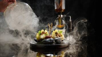 A hand pouring smoke into a smoking device with a bowl of food and rocks.
