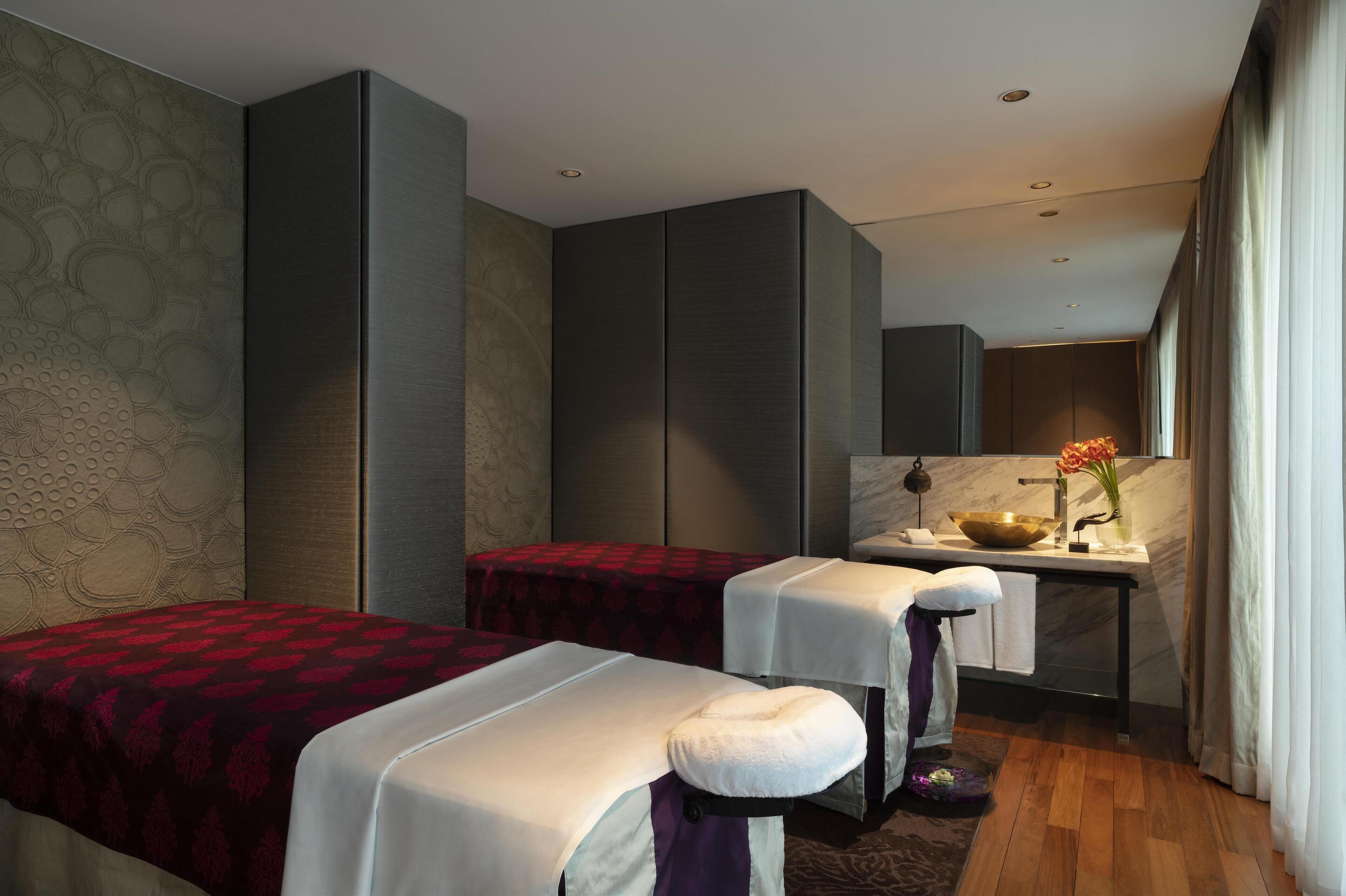 A modern hotel room with two beds, a small desk with a sink, and a large mirror.