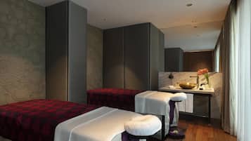 A modern hotel room with two beds, a small desk with a sink, and a large mirror.