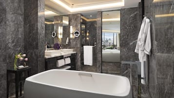 Een moderne badkamer met een vrijstaand bad, een wastafel met spiegel en uitzicht op een stadsbeeld door een geopende deur.