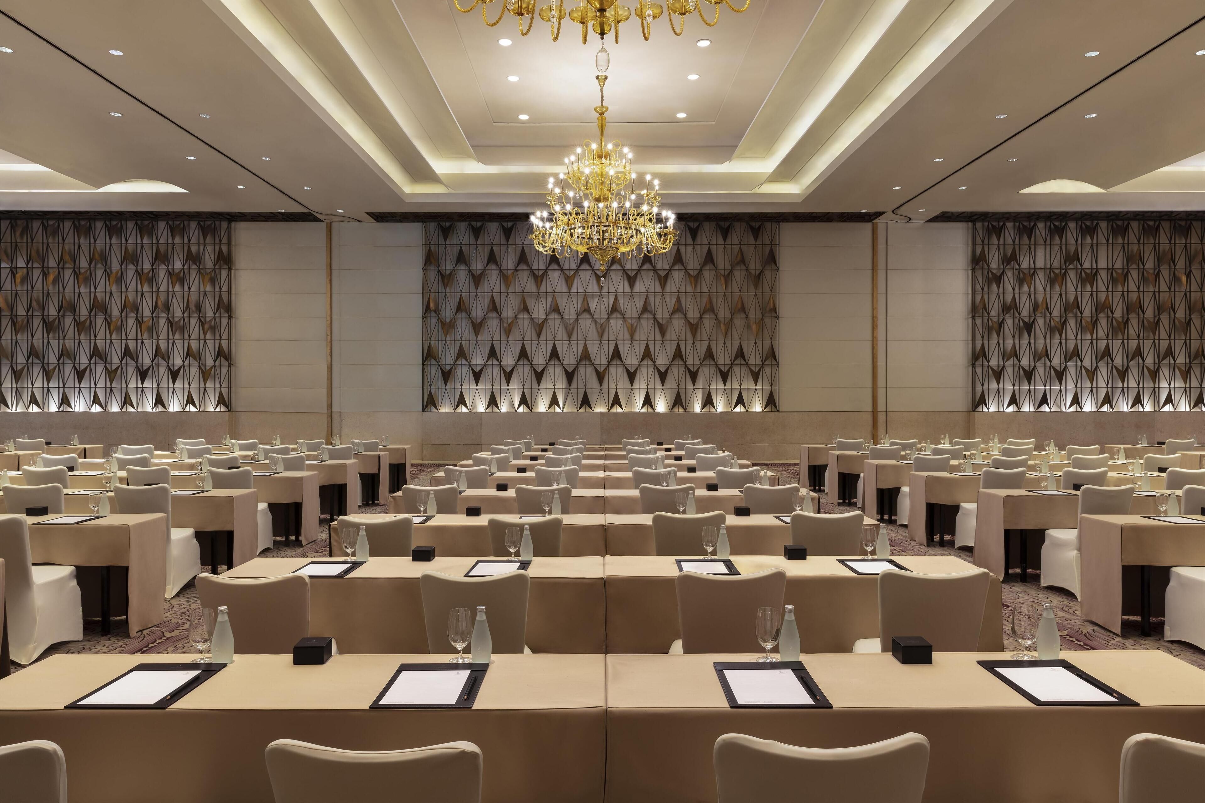 A conference room with rows of tables and chairs, a chandelier, and patterned walls.