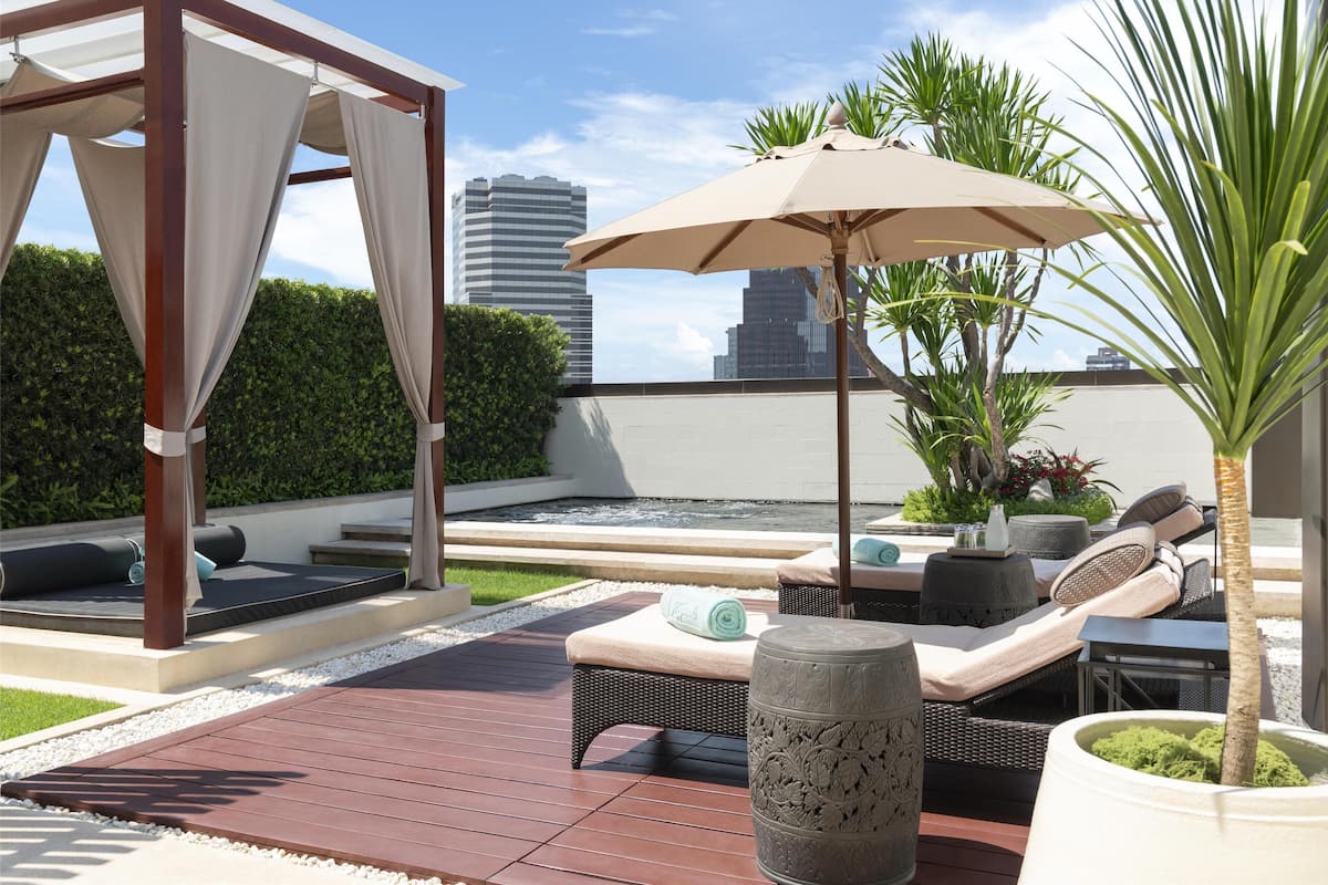 Eine Dachterrasse mit Pergola, Sitzgelegenheiten im Freien, einem Wasserspiel und Blick auf Stadtgebäude.