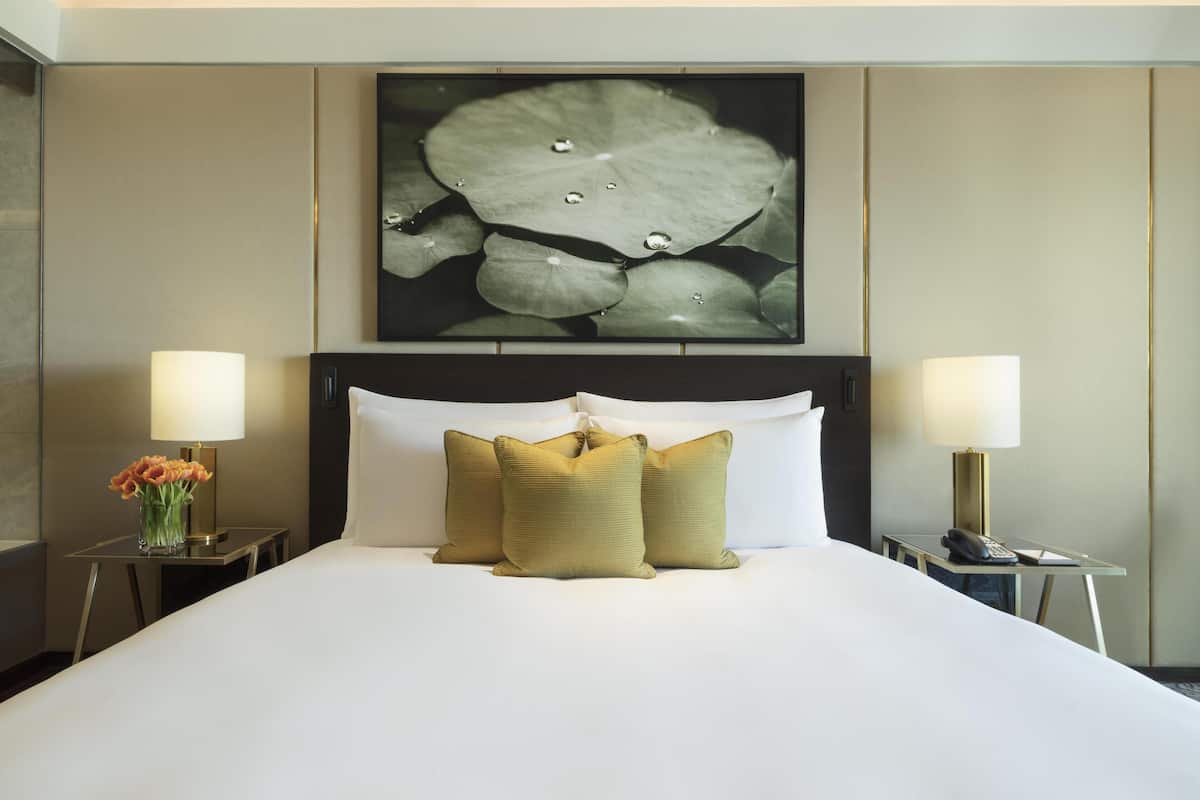 Ein Hotelzimmer mit einem großen Bett, zwei Nachttischen, einer Ablagefläche, einem Wandbild und einer Vase mit Blumen.