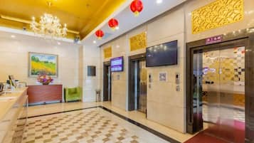 A hotel lobby with a checkered floor, a reception desk, a green seating area, and two elevators.