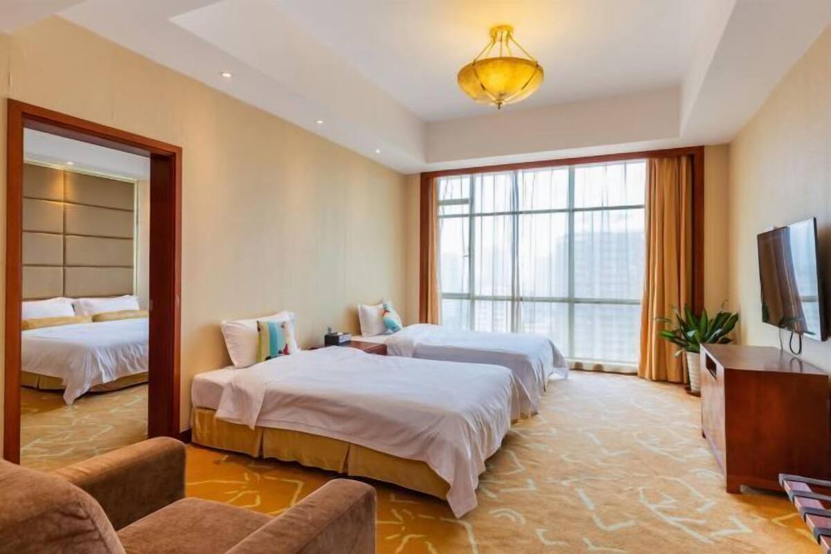 A hotel room with two beds, a TV, a desk, and a large window.