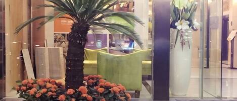A reception area with a palm tree, a large vase of flowers, and a green chair.