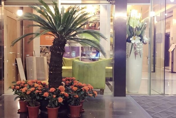 A reception area with a palm tree, a large vase of flowers, and a green chair.