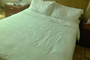 Una cama con ropa blanca, una mesita de noche de madera con una lámpara y un teléfono.