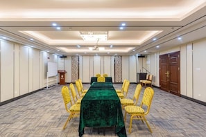 Un salón de conferencias con una larga mesa, sillas amarillas, un mantel verde y una pizarra.