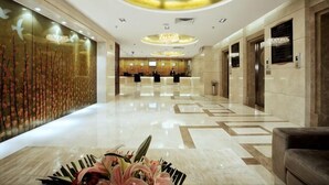A hotel lobby with a reception desk, elevators, and a decorative floral arrangement on the floor.