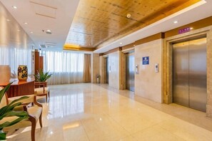 Un vestíbulo de hotel con mostrador de recepción, zona de estar, ascensores y suelo pulido.