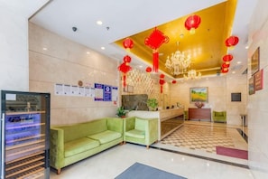 Eine Hotelhalle mit einer Rezeption, einem grünen Sofa, einem Chandelier und roten Laternen.