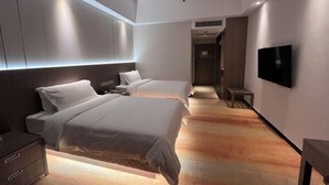 A modern hotel room with two beds, a TV, and a wooden floor.