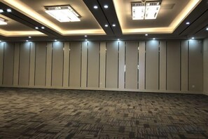Une grande chambre d’hôtel vide, avec un tapis à motifs, un éclairage encastré et une rangée de panneaux verticaux sur le mur.