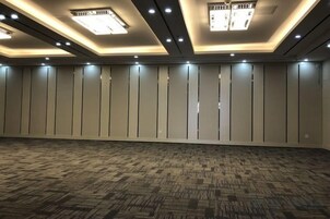 Amplia habitación de hotel vacía con alfombra estampada, iluminación empotrada y una fila de paneles verticales en la pared.