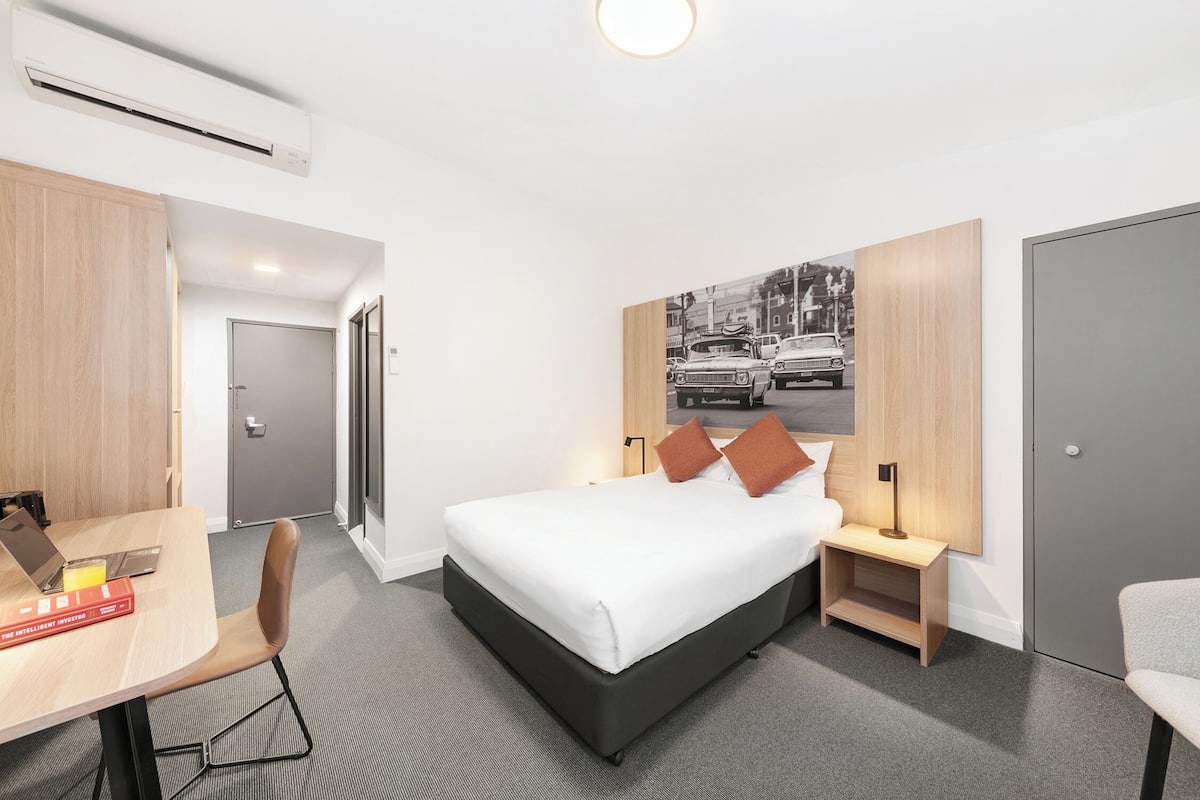 A modern hotel room with a bed, bedside tables, a desk, and a chair.