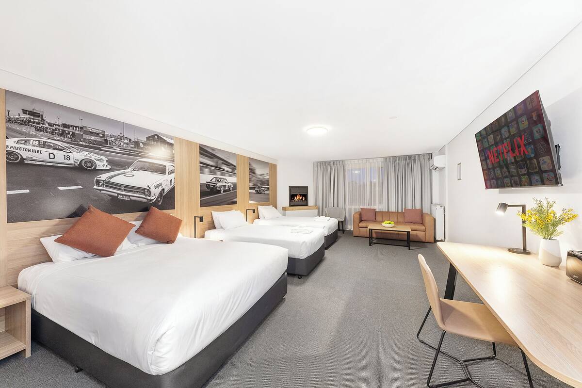 A hotel room with three beds, a desk, a couch, and a TV mounted on the wall.