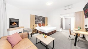 Une chambre d’hôtel moderne, équipée d’un lit, d’un canapé, d’un bureau, d’une cheminée et ornée d’un grand tableau au mur.