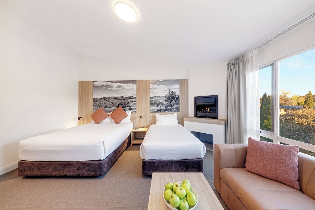 A hotel room with two beds, a sofa, a TV, and a large window with a view.