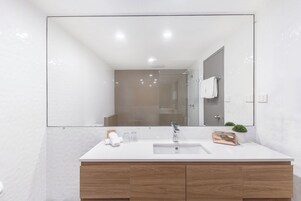 Un baño moderno con un espejo grande, tocador blanco y una pequeña planta en maceta.