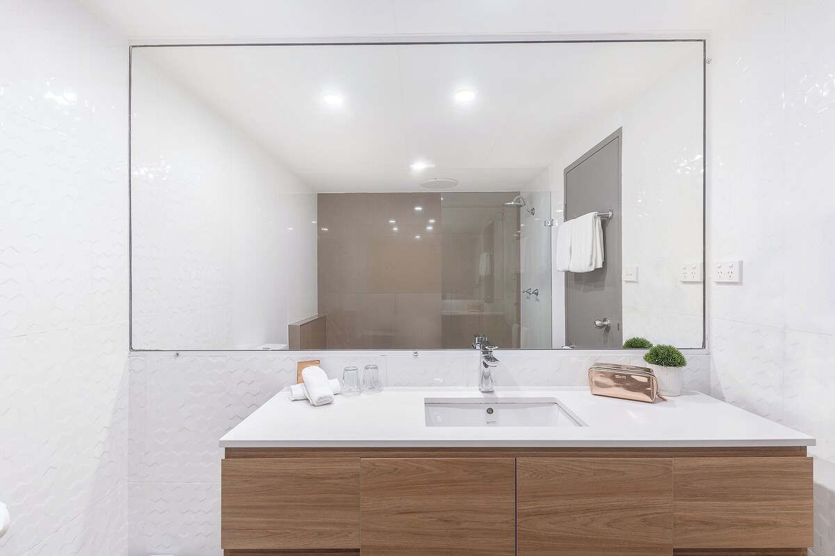 A modern bathroom with a large mirror, white vanity, and a small potted plant.