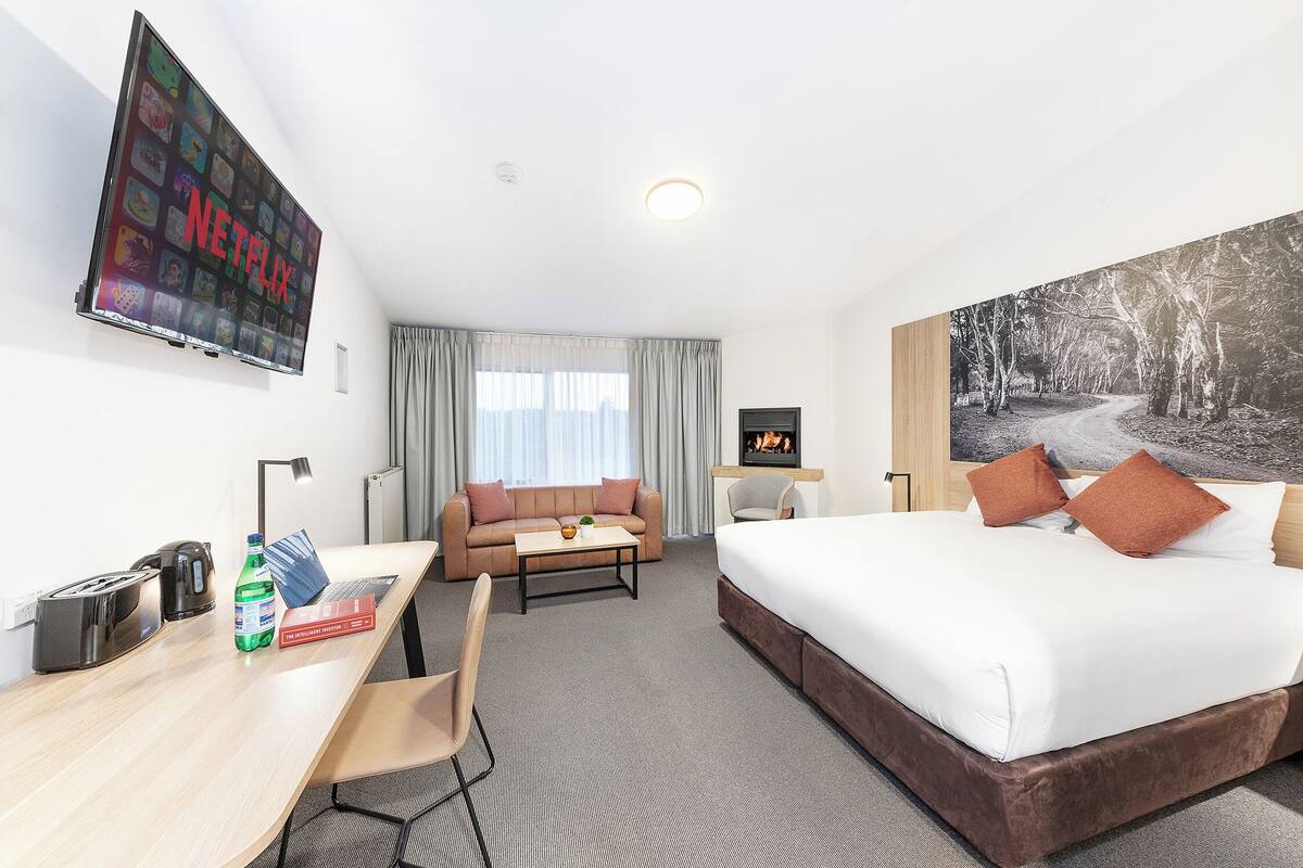 A hotel room with a bed, a desk with a computer, a TV, and a painting on the wall.