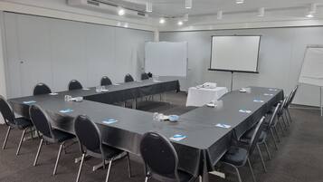 Ein Konferenzraum mit einem langen Tisch, Stühlen, einer Whiteboard und einem Projektor.