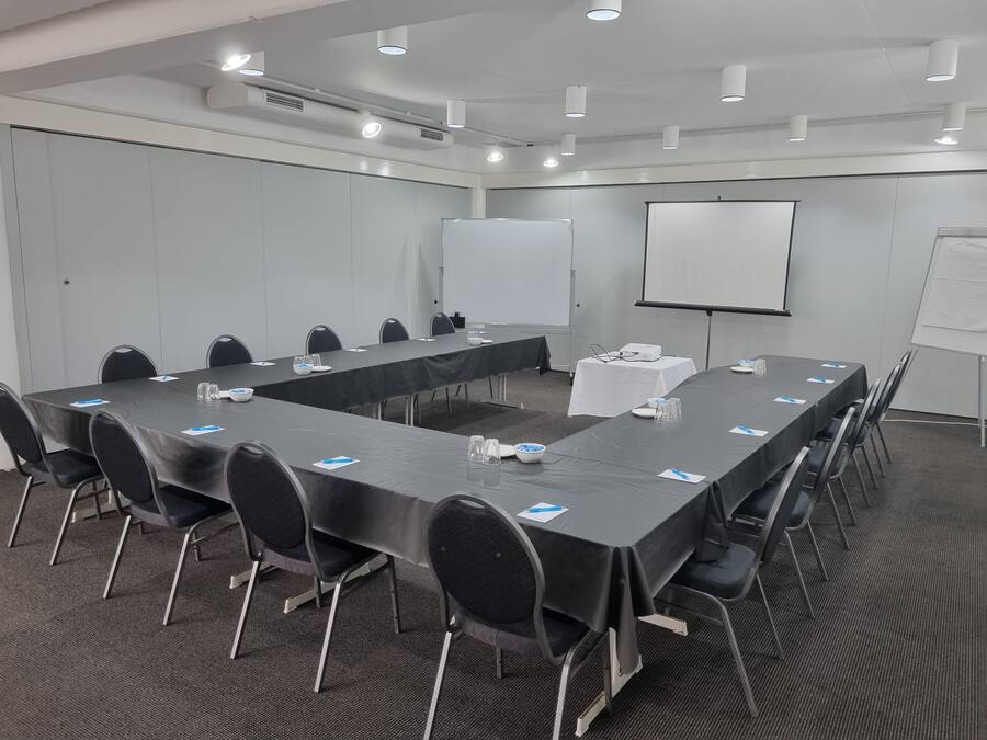 Un salón de conferencias con una larga mesa, sillas, una pizarra y un proyector.