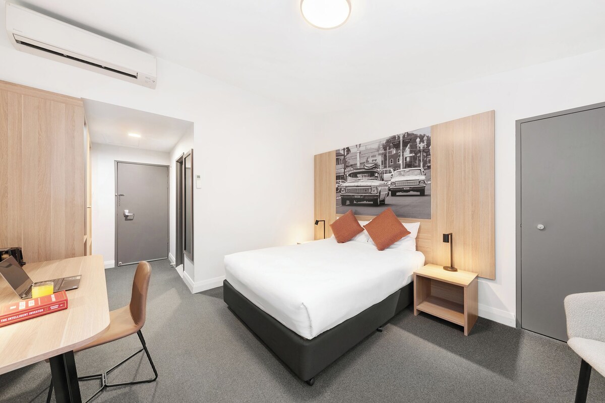 A modern hotel room with a bed, bedside tables, a desk, and a chair.
