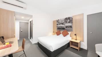 A modern hotel room with a bed, bedside tables, a desk, and a chair.