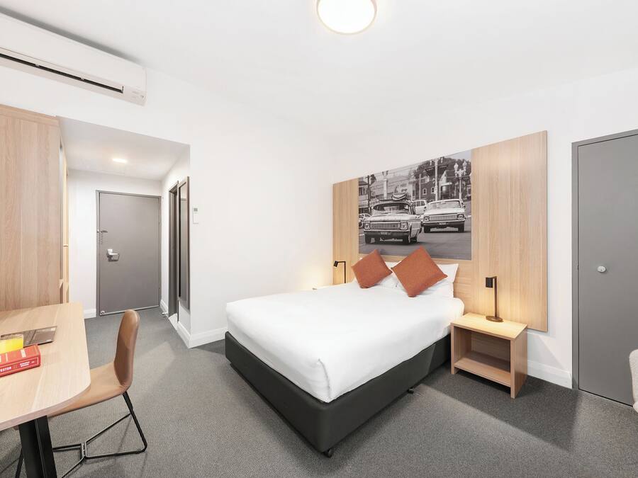 A modern hotel room with a bed, bedside tables, a desk, and a chair.