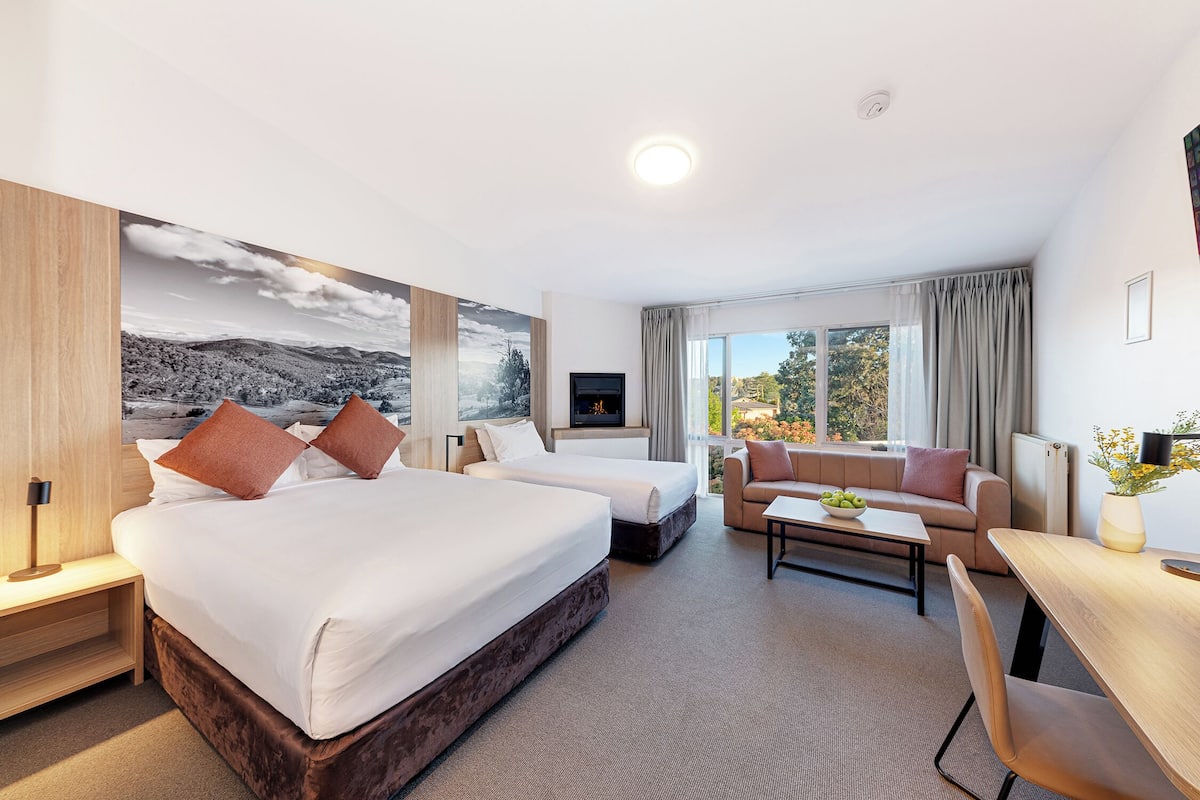 A hotel room with a large bed, a sofa, a desk, and a TV.