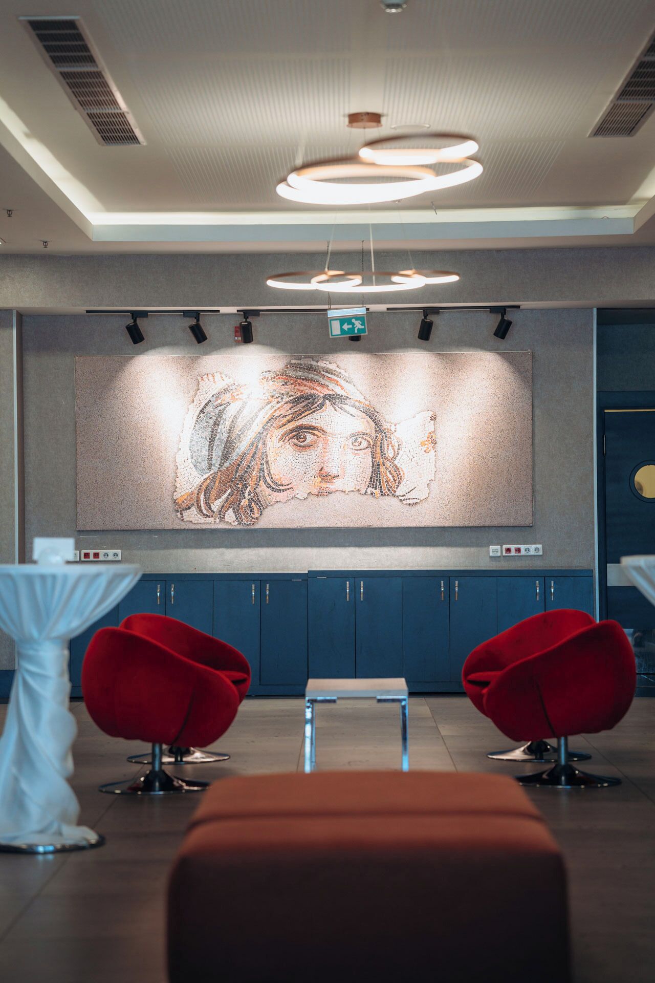 A modern interior with a large mosaic artwork on the wall, blue cabinets, and red chairs.