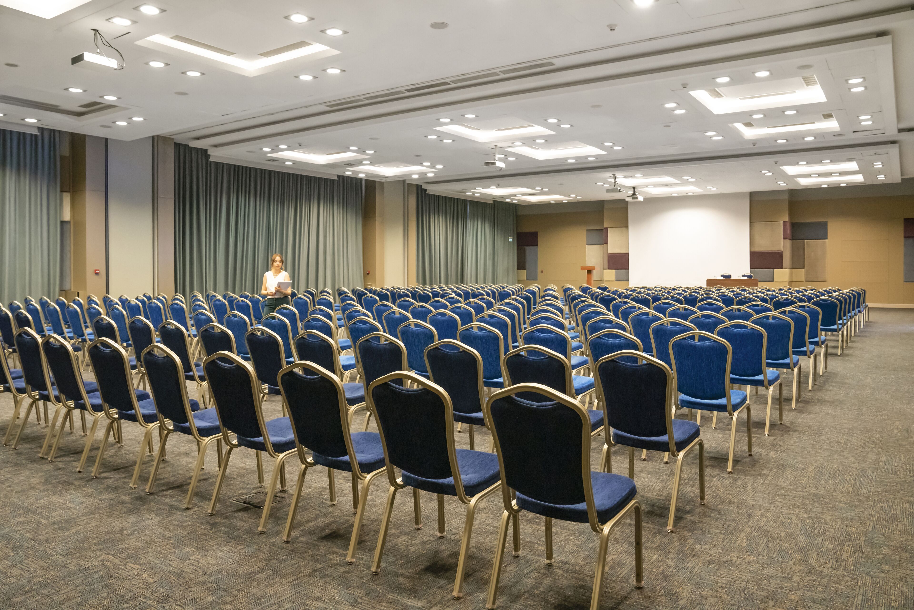Un salón de conferencias con filas de sillas azules y un atril al frente.